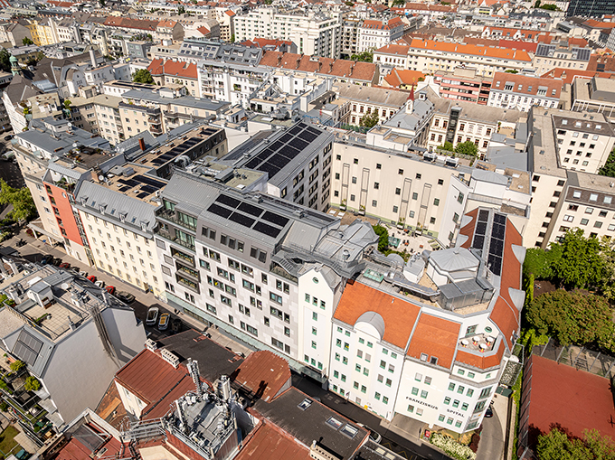 Außenansicht des Franziskus Spitals Margareten bei Tageslicht, mit modernem Eingangsbereich und sichtbarem Spitalschriftzug. Gut sichtbar - die neue PV-Anlage am Dach des Hauses.